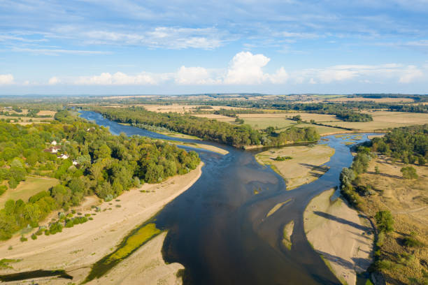 Cette photo a été prise en France, en Bourgogne, dans la Nièvre, au Bec d'Allier. Cette photo montre la Loire au milieu de la campagne française à la fin des moissons avec des forêts, des champs et des routes et un ciel bleu remplit de nuages.